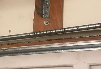Close-up view of a dented garage door panel and broken spring before repair at a National City, CA home.