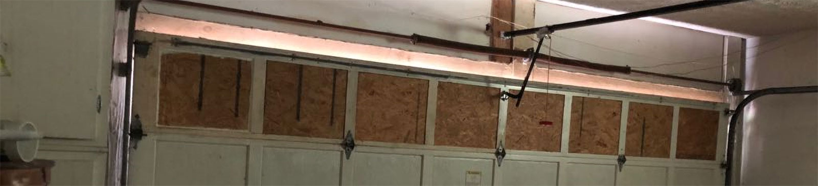Close-up view of a dented garage door panel and broken spring before repair at a National City, CA home.